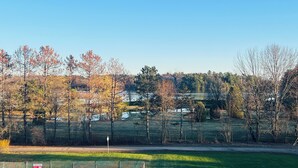 A rural landscape with a clear sky, trees with autumn foliage, and a fenced area.