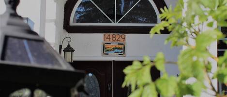 A building entrance with a large arched window, a door with a sign above it, and a potted plant in the foreground.