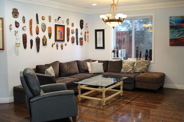 A living room with a sectional sofa, a glass coffee table, and a wall decorated with various cultural artifacts. - Sweet Dreams B&B (Sherman Oaks)