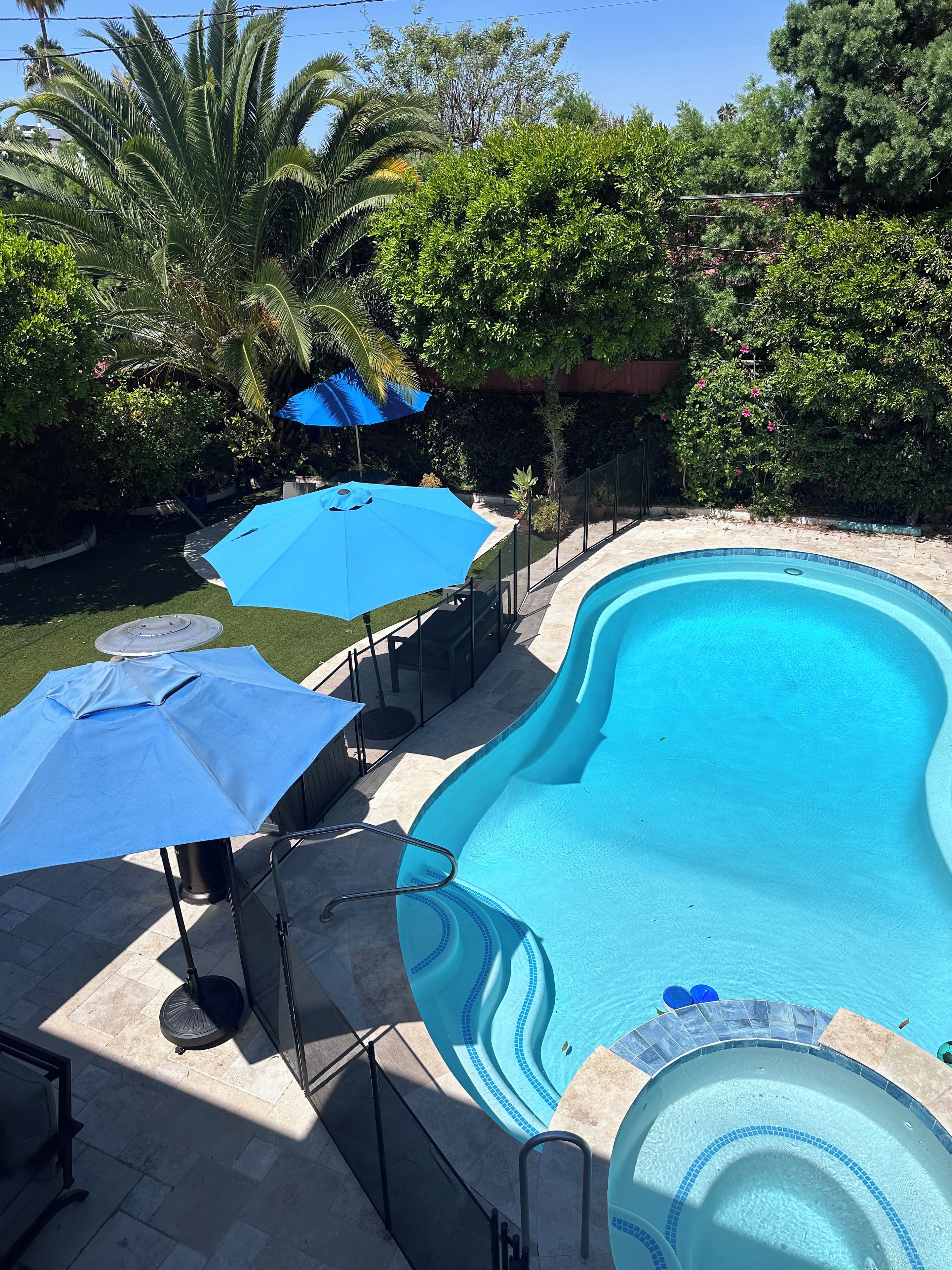 Een zwembad met een golvende rand, omgeven door een terras met parasols en een kleine jacuzzi.
