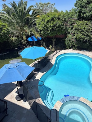 A swimming pool with a wavy edge, surrounded by a patio area with umbrellas and a small hot tub. - Sweet Dreams B&B (Sherman Oaks)