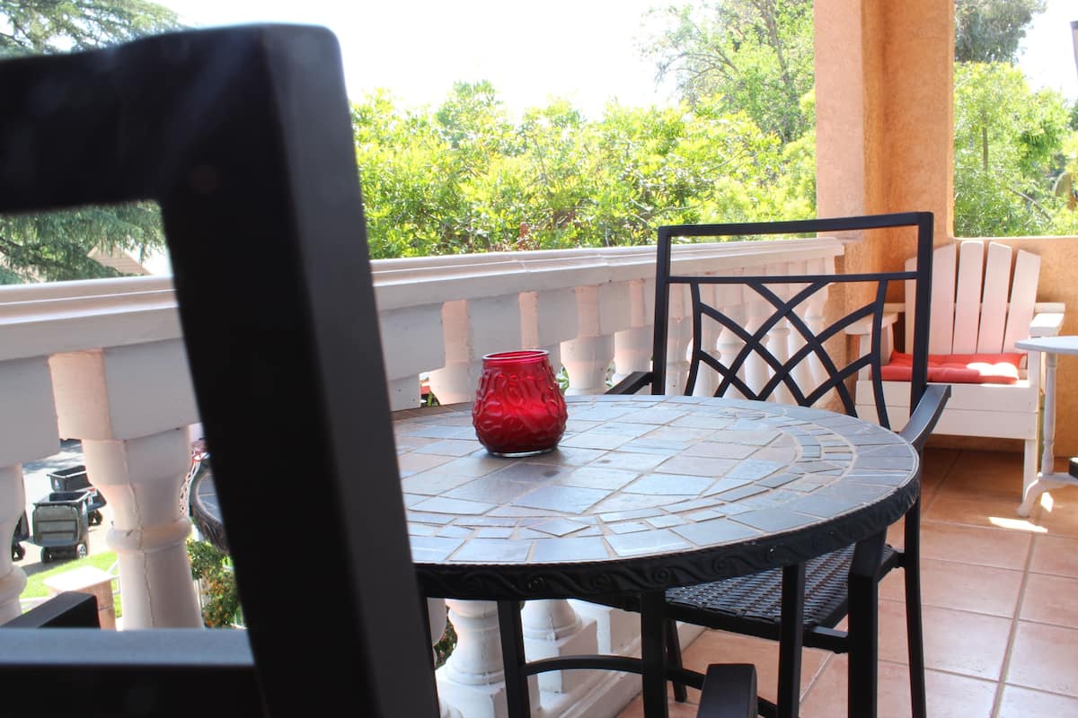 A round table with a mosaic tile design, surrounded by black chairs with a lattice backrest. A red vase is placed on the table.