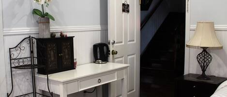 A bedroom with a white dresser, a black metal chair, a white lamp, and a staircase leading to another room.