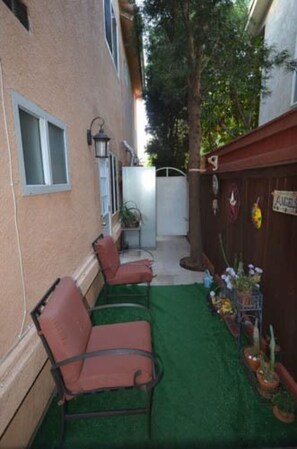 outdoor space with artificial turf, two chairs, and a garden view.