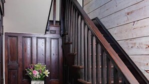 Uma escada de madeira com corrimão, uma pequena mesa com um vaso de flores e um porta-retrato na parede.