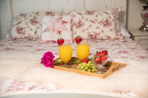 A bed with floral bedding and pillows, a tray with fruit and juice glasses.