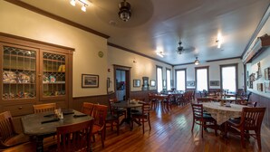 A spacious dining area with wooden flooring and multiple tables and chairs.