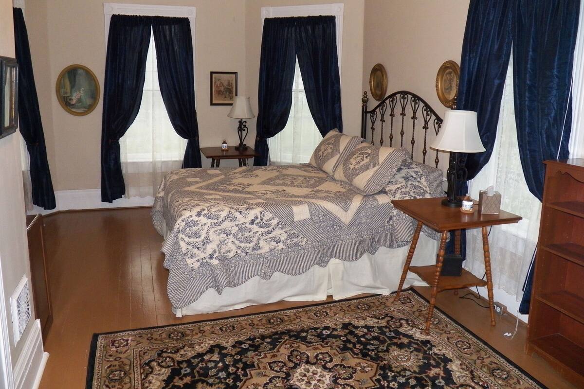 A bedroom with a large bed, two bedside tables, a nightstand, a wooden dresser, and a patterned rug.