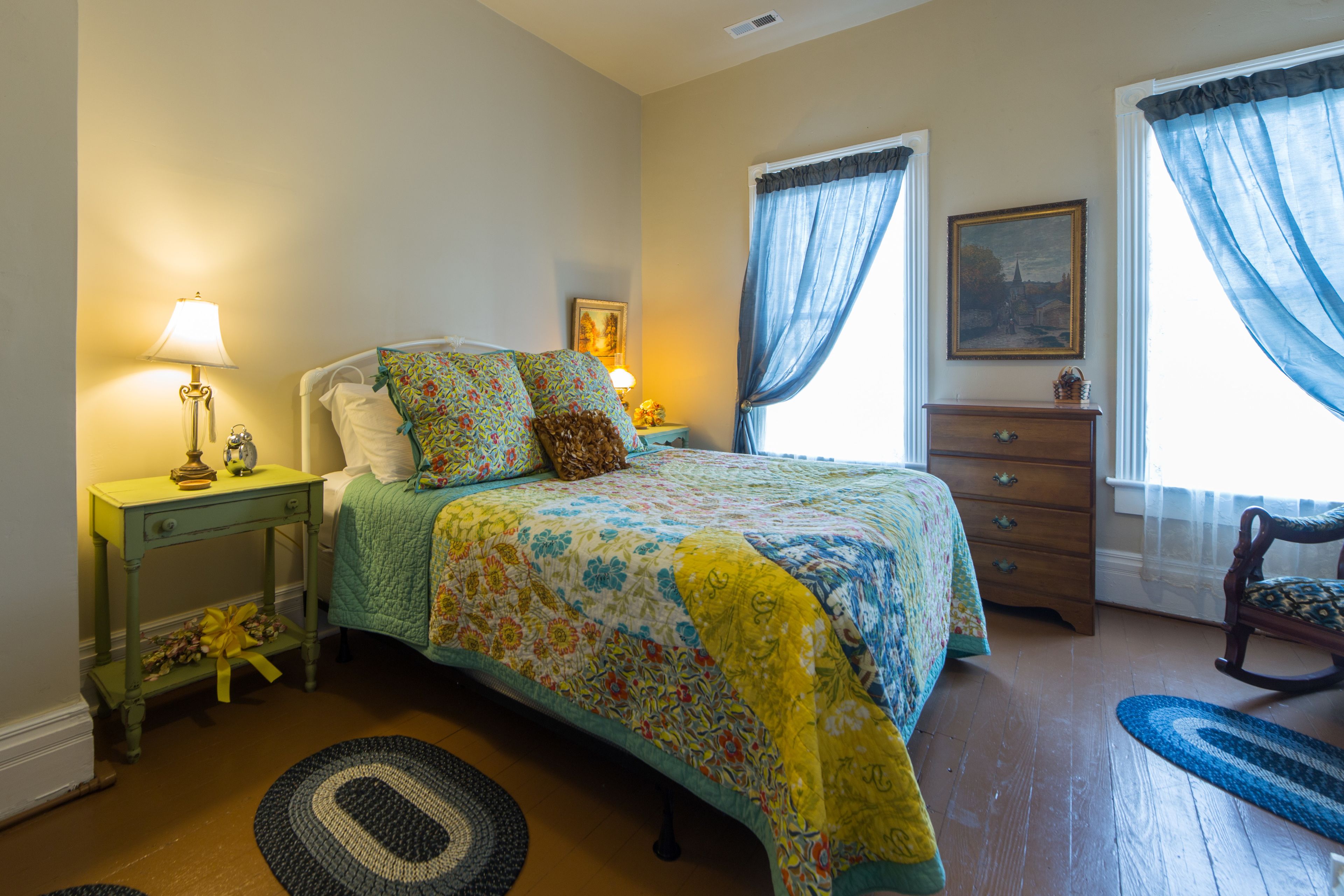 A bedroom with a bed, a nightstand, a dresser, a chair, and a window with curtains.