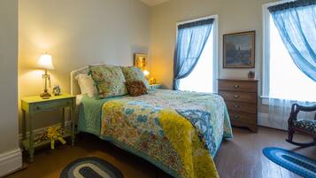 A bedroom with a bed, a nightstand, a dresser, a chair, and a window with curtains.