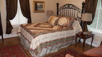 A neatly made bed with a quilt, a bedside table with a lamp, and a chair.