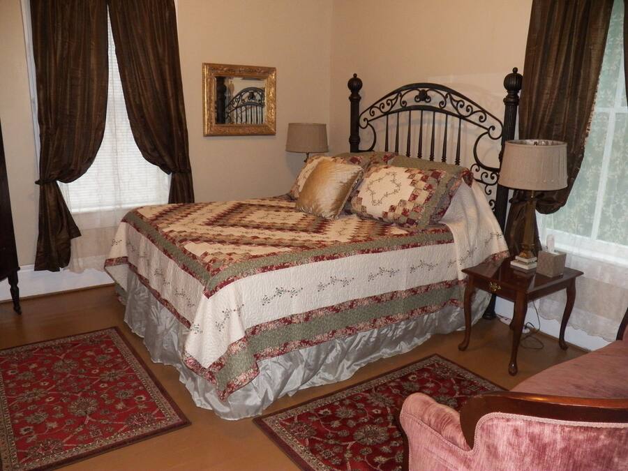 En pænt redt seng med et quiltet dynebetræk, et sengebord med en lampe, og en stol.