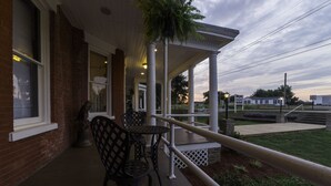 A covered outdoor seating area with a brick building, a statue, and a view of a grassy field.
