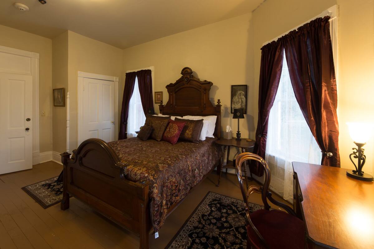 A bedroom with a wooden bed, a desk, a chair, and a nightstand.