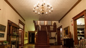 A spacious foyer with a patterned carpet, wooden staircase, and a chandelier.
