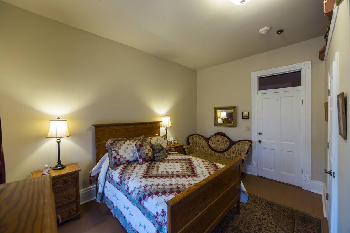 A bedroom with a wooden bed, two bedside lamps, a nightstand, a chair, a door, and a mirror on the wall.