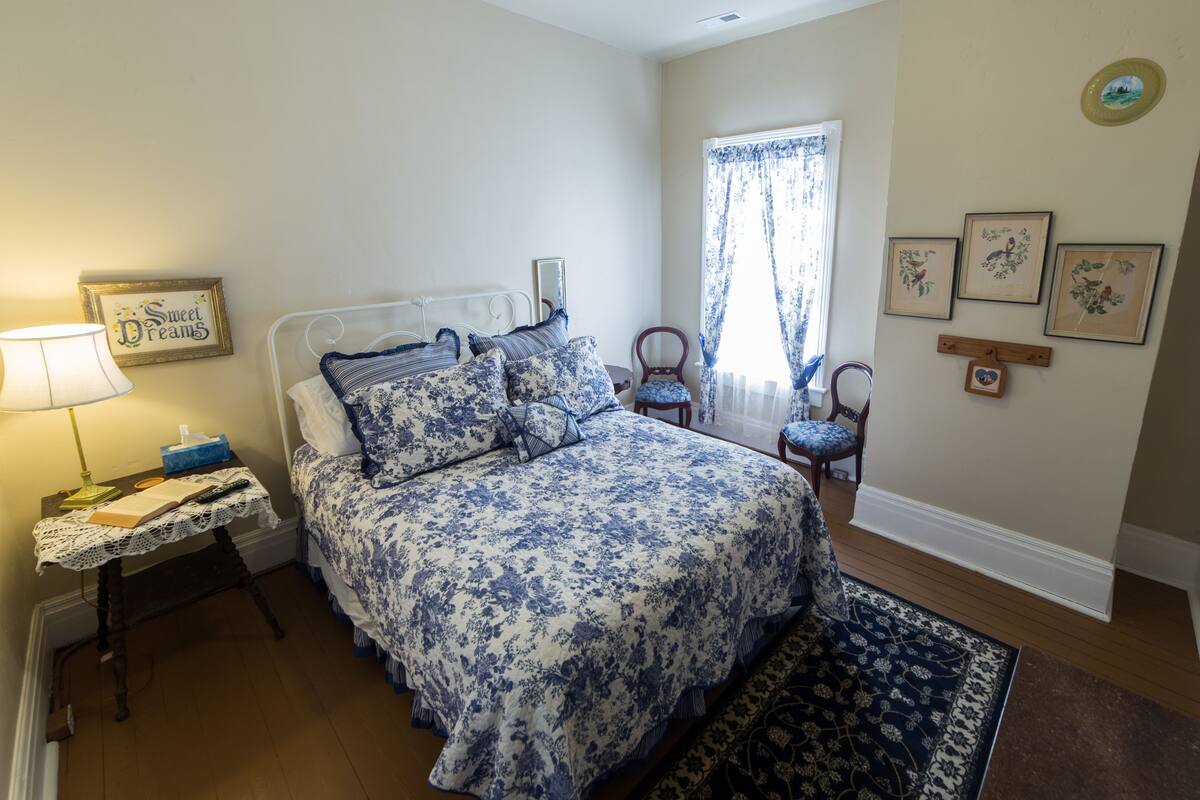 A bedroom with a bed, bedside table, lamp, and a window with curtains.