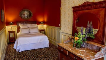 A hotel room with a large bed, a wooden dresser with a mirror, and a floral arrangement on the dresser.