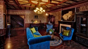 Une pièce au décor traditionnel, avec un plafond en bois, un canapé bleu, un fauteuil bleu, une cheminée et une statue de chat.
