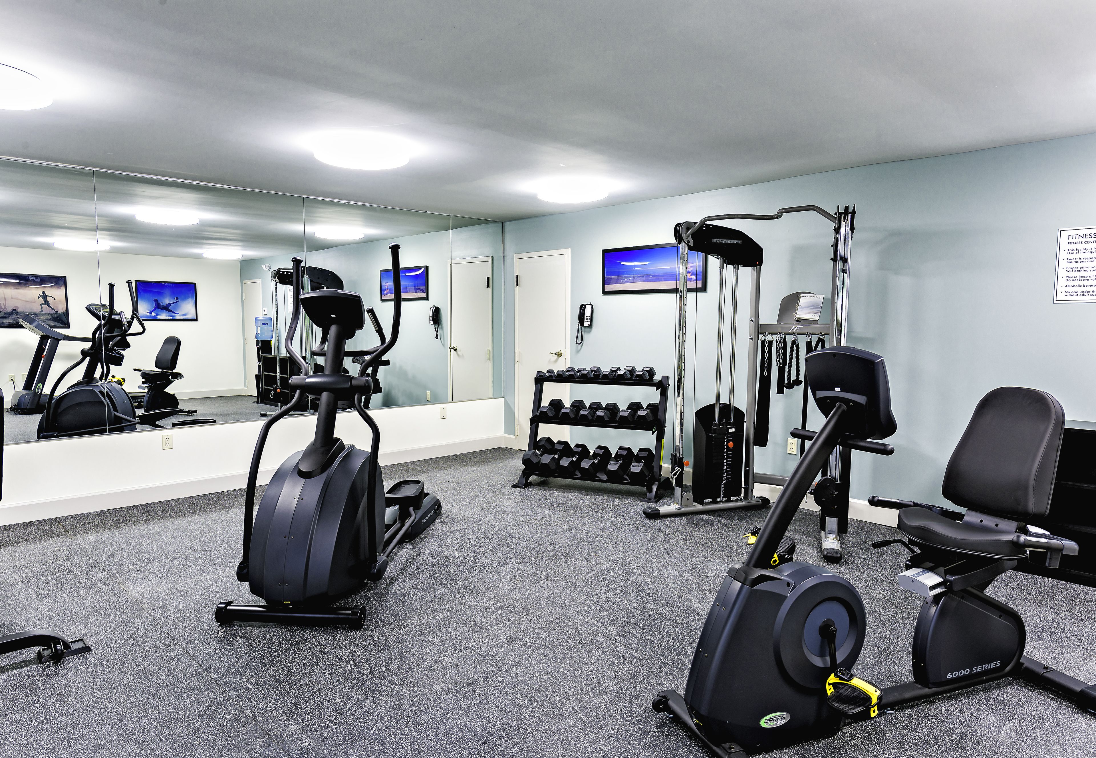 A gym with cardio equipment, dumbbells, and a weight rack.
