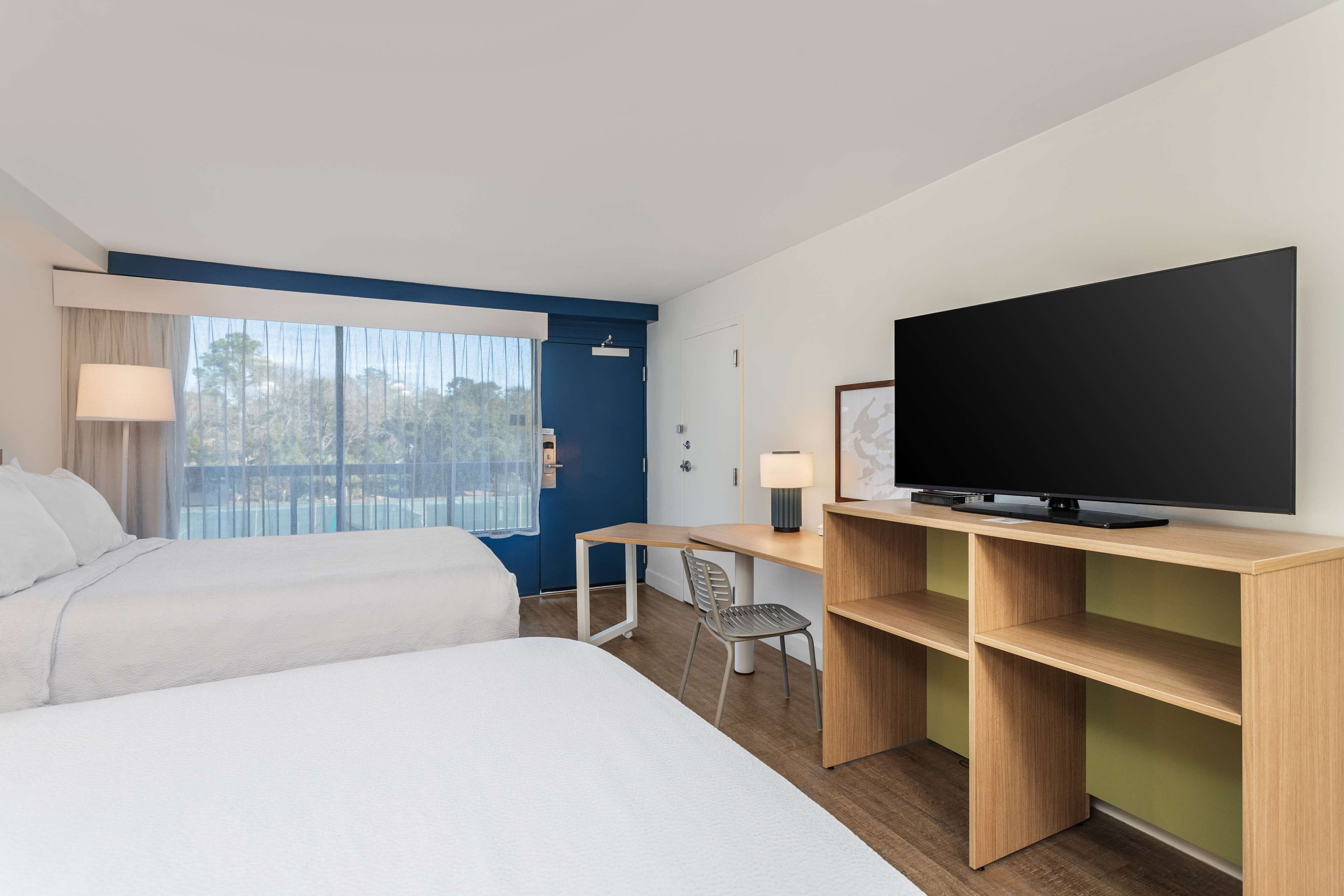 Een hotelkamer met twee bedden, een bureau met stoel, een televisie en een raam met gordijnen.