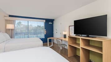 Habitación de hotel con dos camas, un escritorio con silla, televisor y ventana con cortinas.