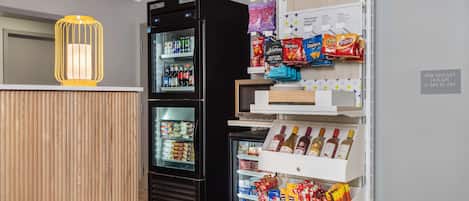 Eine Hotelhalle mit einem Holzbüro, einem schwarzen Kühlschrank mit Getränken, Snackregalen und einem Weinkühler.