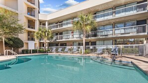 A pool area with lounge chairs and a building with balconies. - Spark By Hilton Hilton Head Island (Hilton Head Island)