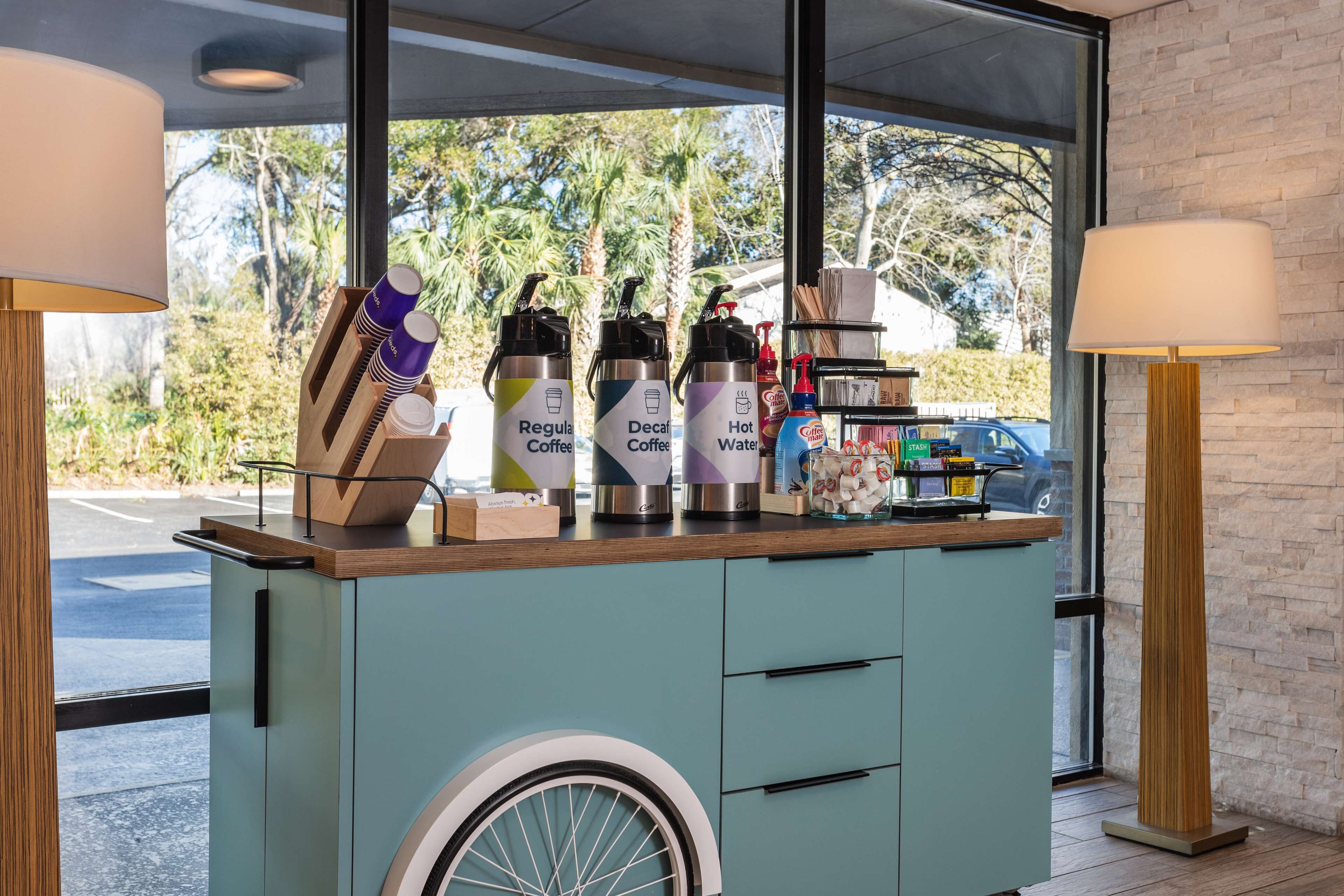A counter with coffee dispensers labeled 'Regular Coffee,' 'Decaf Coffee,' and 'Hot Water.' There are also paper cups and a small shelf with various items.