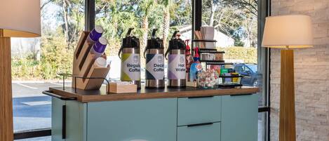A counter with coffee dispensers labeled 'Regular Coffee,' 'Decaf Coffee,' and 'Hot Water.' There are also paper cups and a small shelf with various items.