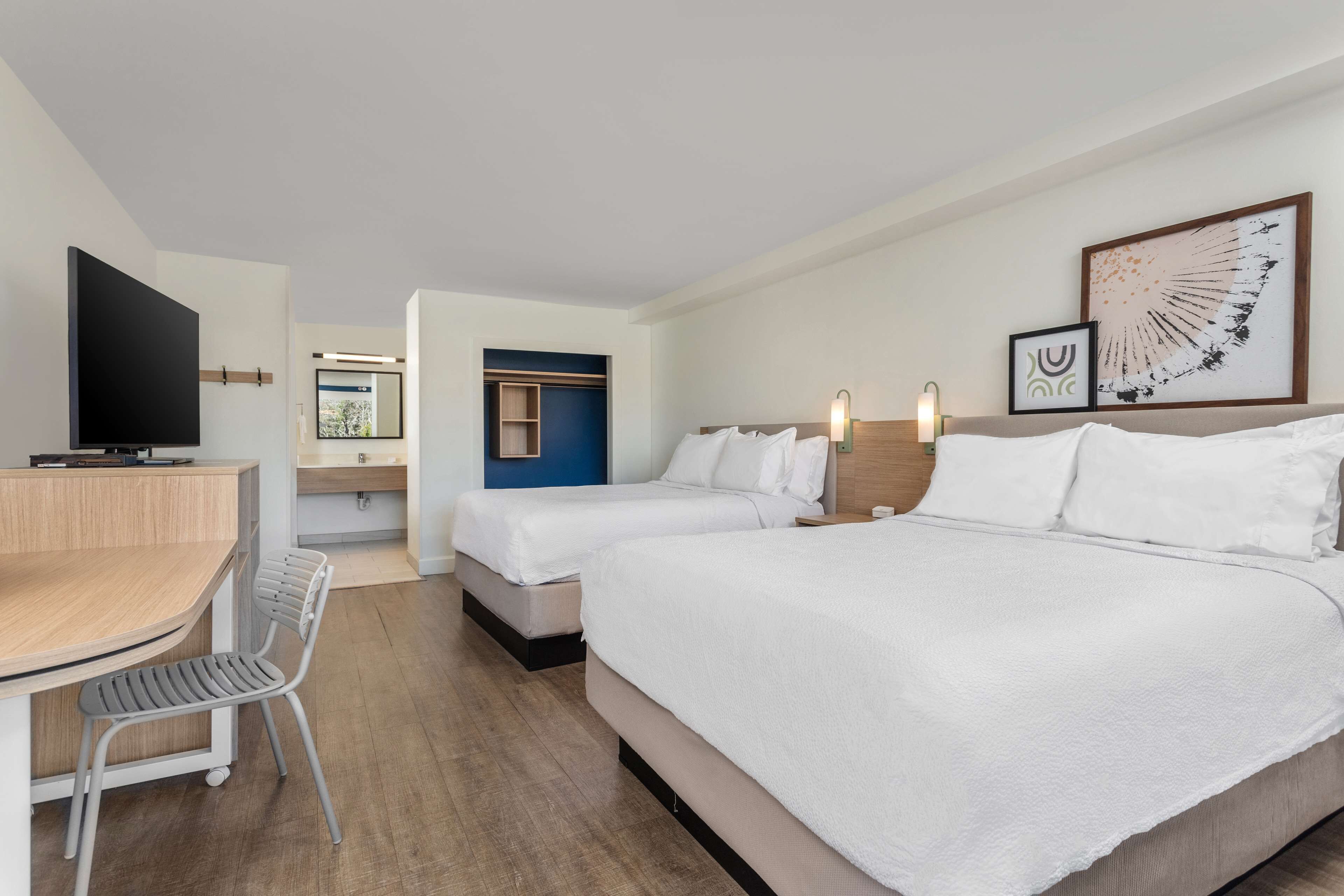 A hotel room with two beds, a desk, a chair, and a TV.