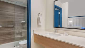 A modern bathroom with a glass shower enclosure, a white toilet, and a large mirror above a sink with a wooden vanity.