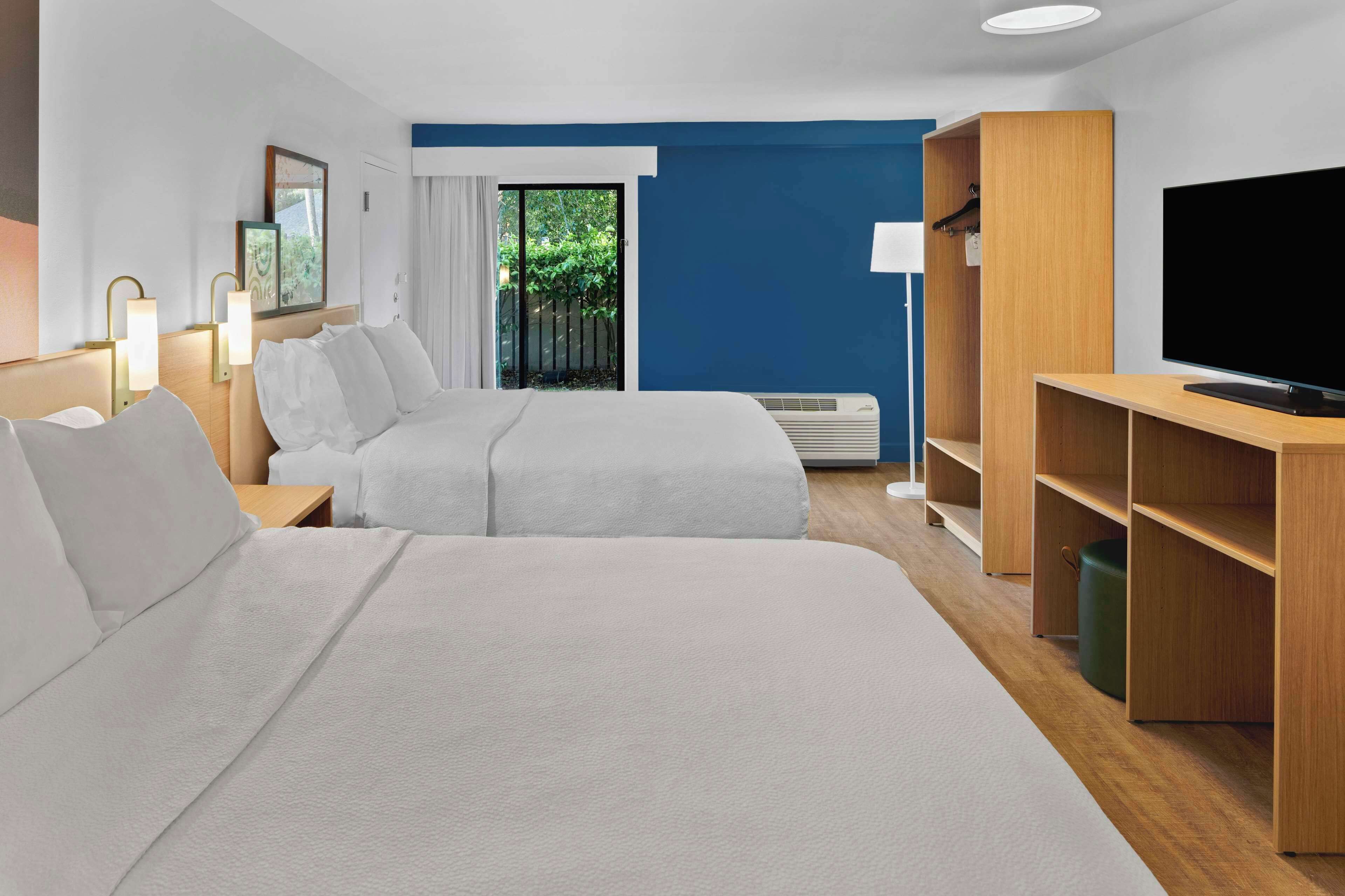 Une chambre d’hôtel avec deux lits, une télévision, une armoire et une fenêtre donnant sur un espace verdoyant.