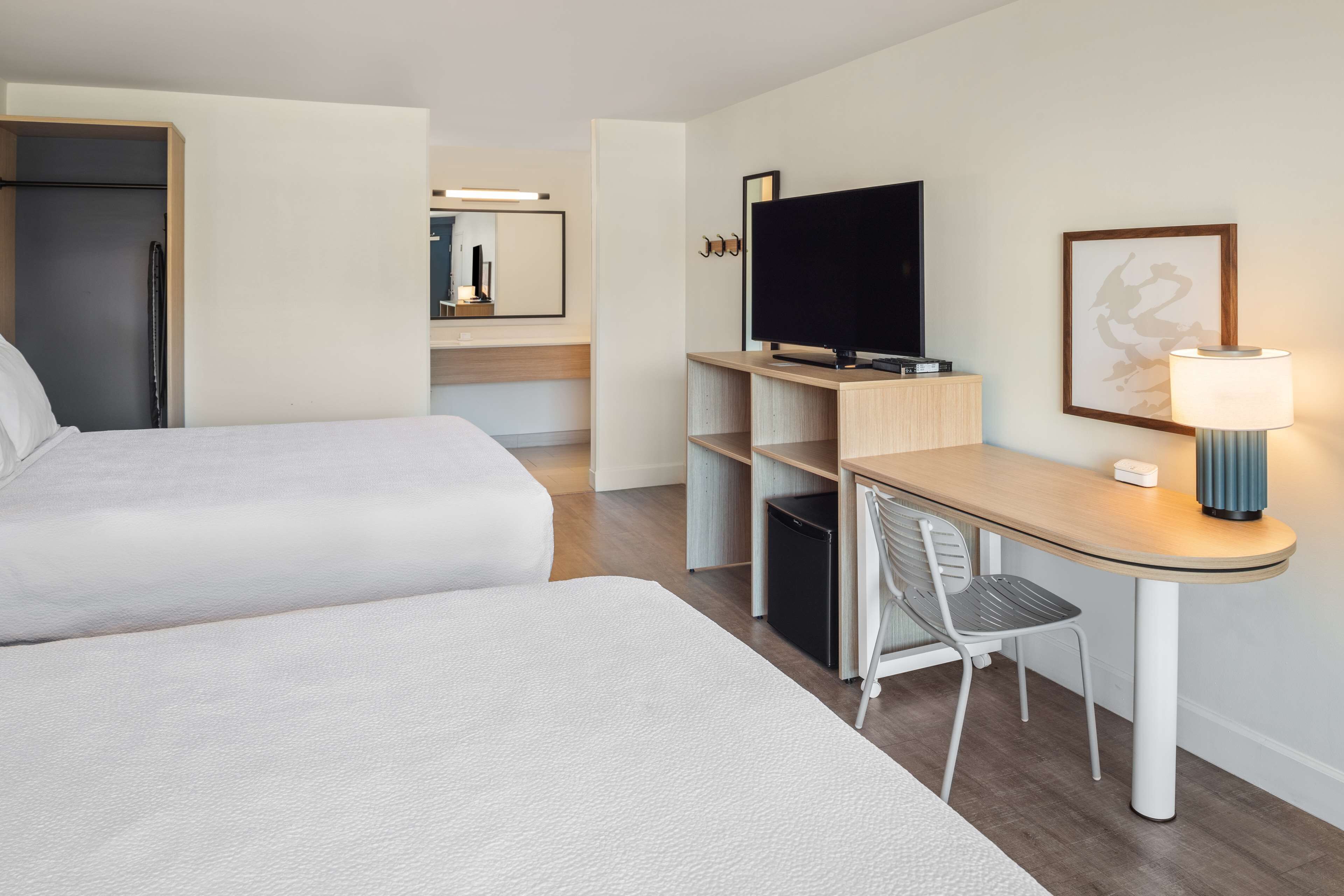 A hotel room with two beds, a desk with a chair, a television, and a lamp.