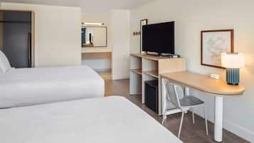 Une chambre d’hôtel avec deux lits, un bureau avec une chaise, une télévision et une lampe.