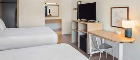 Una habitación de hotel con dos camas, un escritorio con silla, televisor y lámpara.