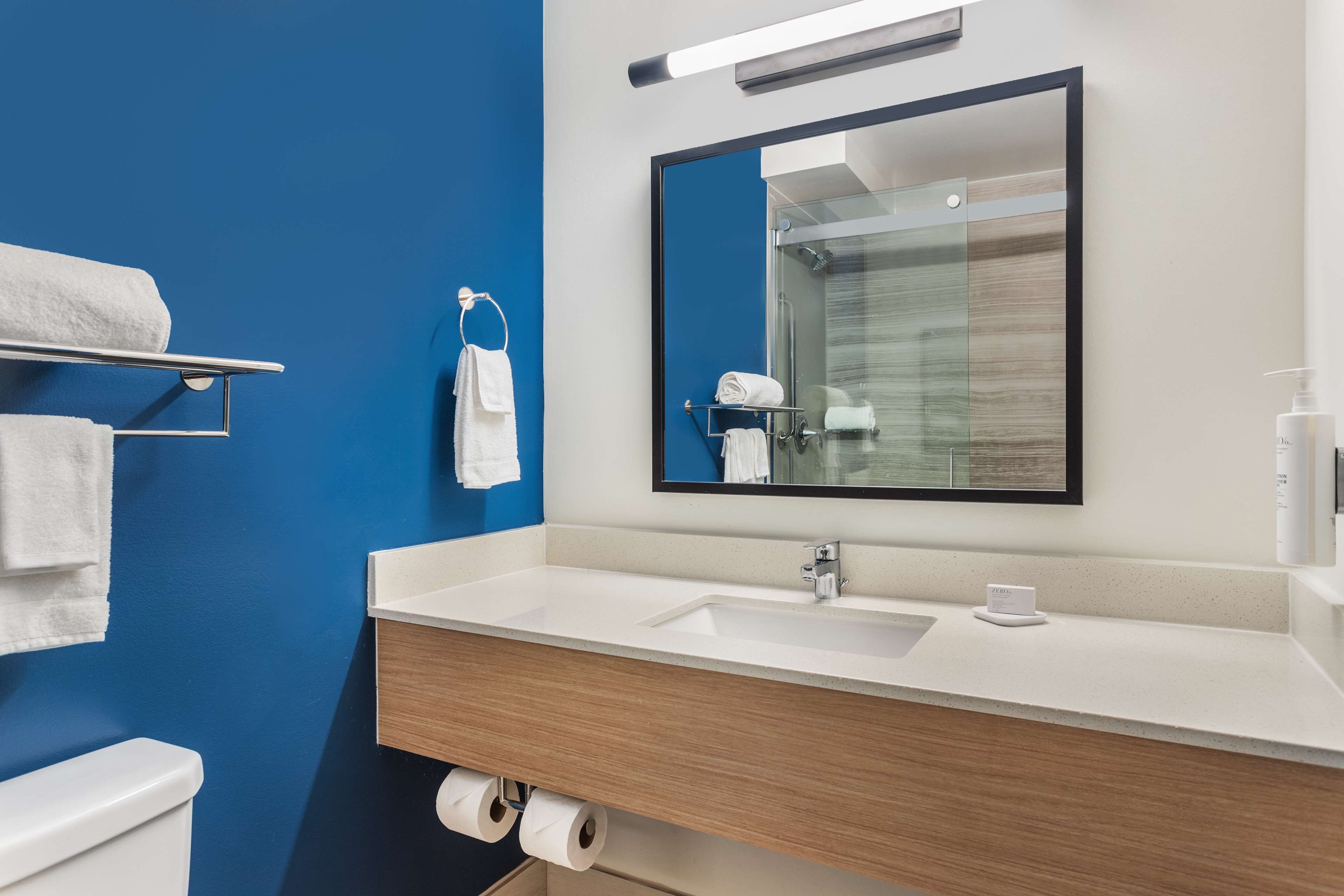 A modern bathroom with a blue accent wall, a white sink, a mirror, and a toilet.
