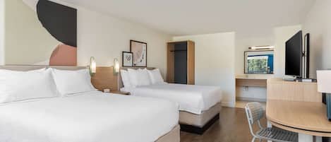 Habitación de hotel con dos camas, un escritorio con silla, televisión y obras de arte en las paredes.