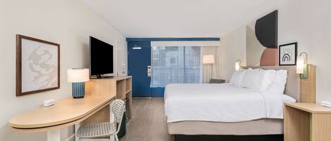 A hotel room with a bed, desk, chair, television, and a door leading to a balcony.