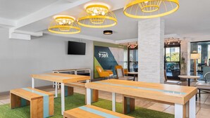 A modern indoor space with wooden tables and benches, a large pillar, and yellow hanging lights. - Spark By Hilton Hilton Head Island (Hilton Head Island)