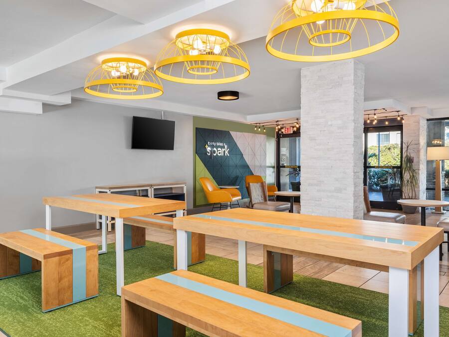 A modern indoor space with wooden tables and benches, a large pillar, and yellow hanging lights.