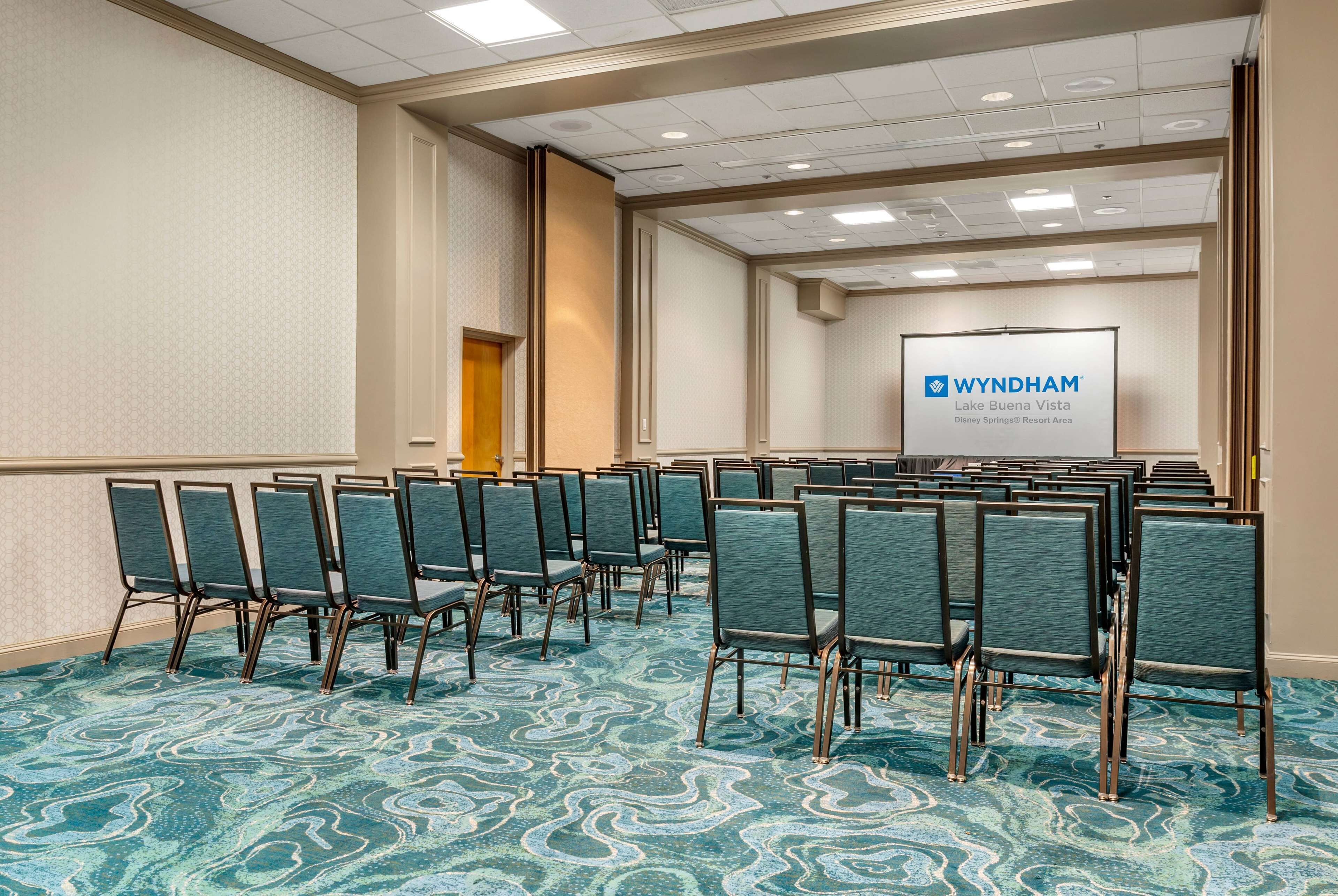 A conference room with rows of chairs, a carpeted floor, and a presentation screen displaying 'WYNDHAM Lake Buena Vista Disney Springs Resort Area'.