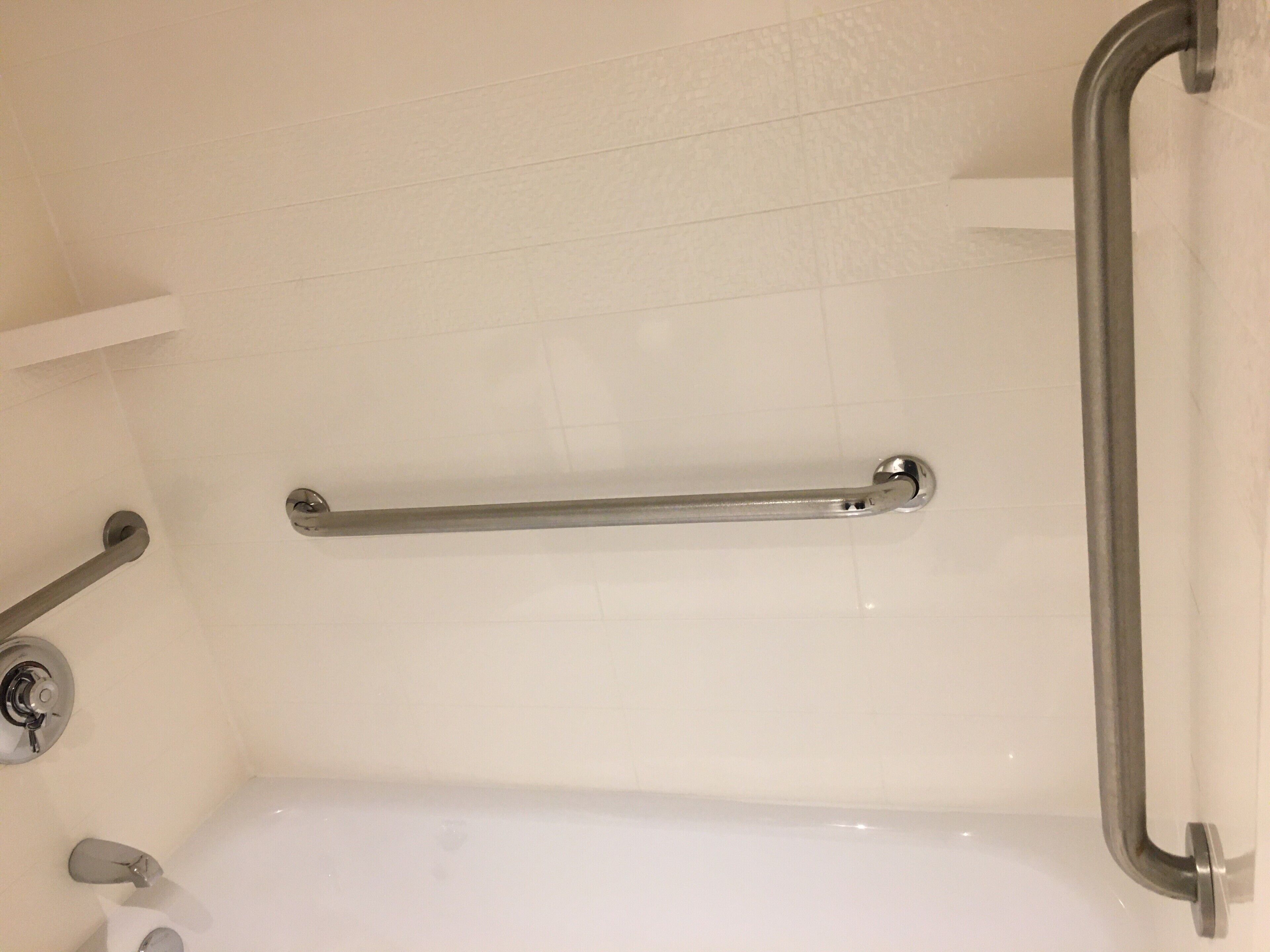 A bathroom with a white bathtub, a grab bar, and a faucet.
