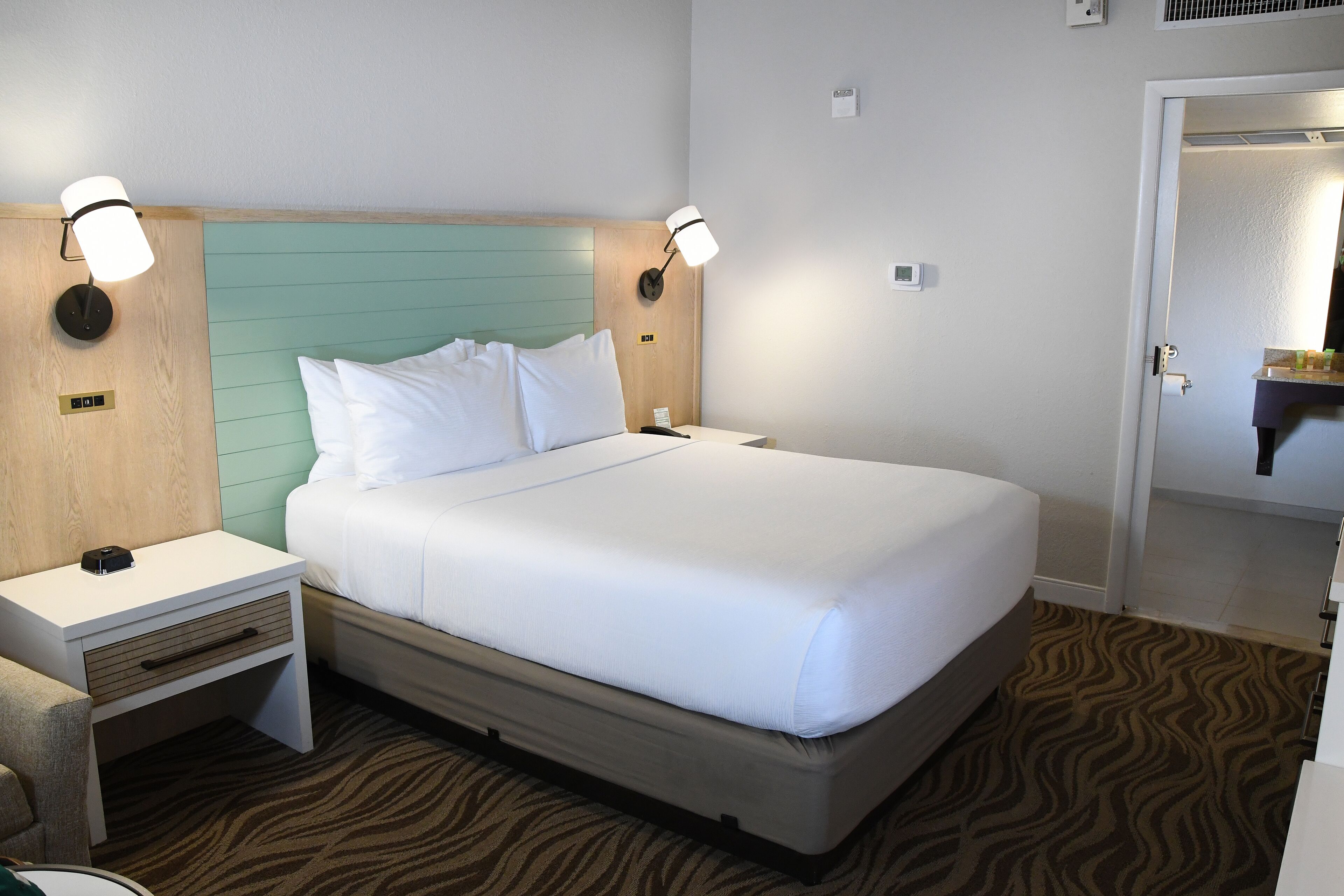 A neatly made bed with white linens, a wooden headboard, and two wall-mounted nightstands with lamps.
