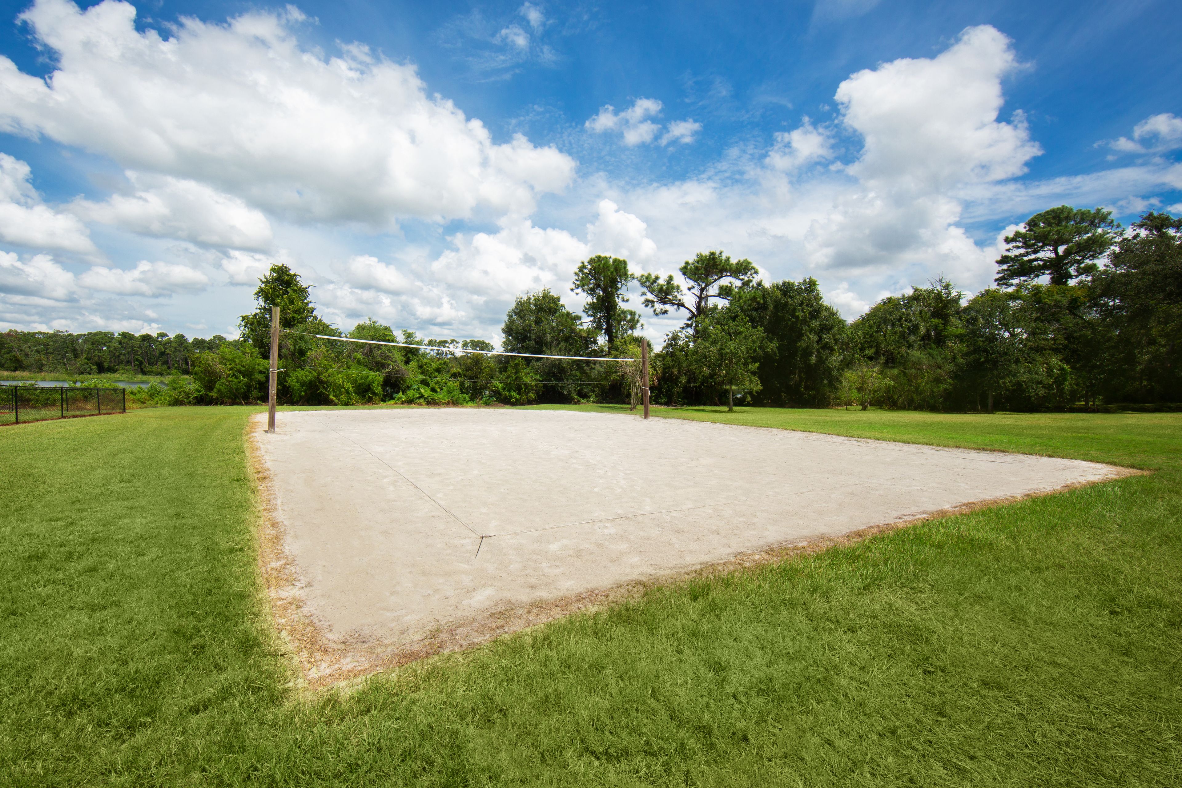 Un terrain de volleyball en plein air, avec un filet, entouré d’herbe verte et d’arbres.