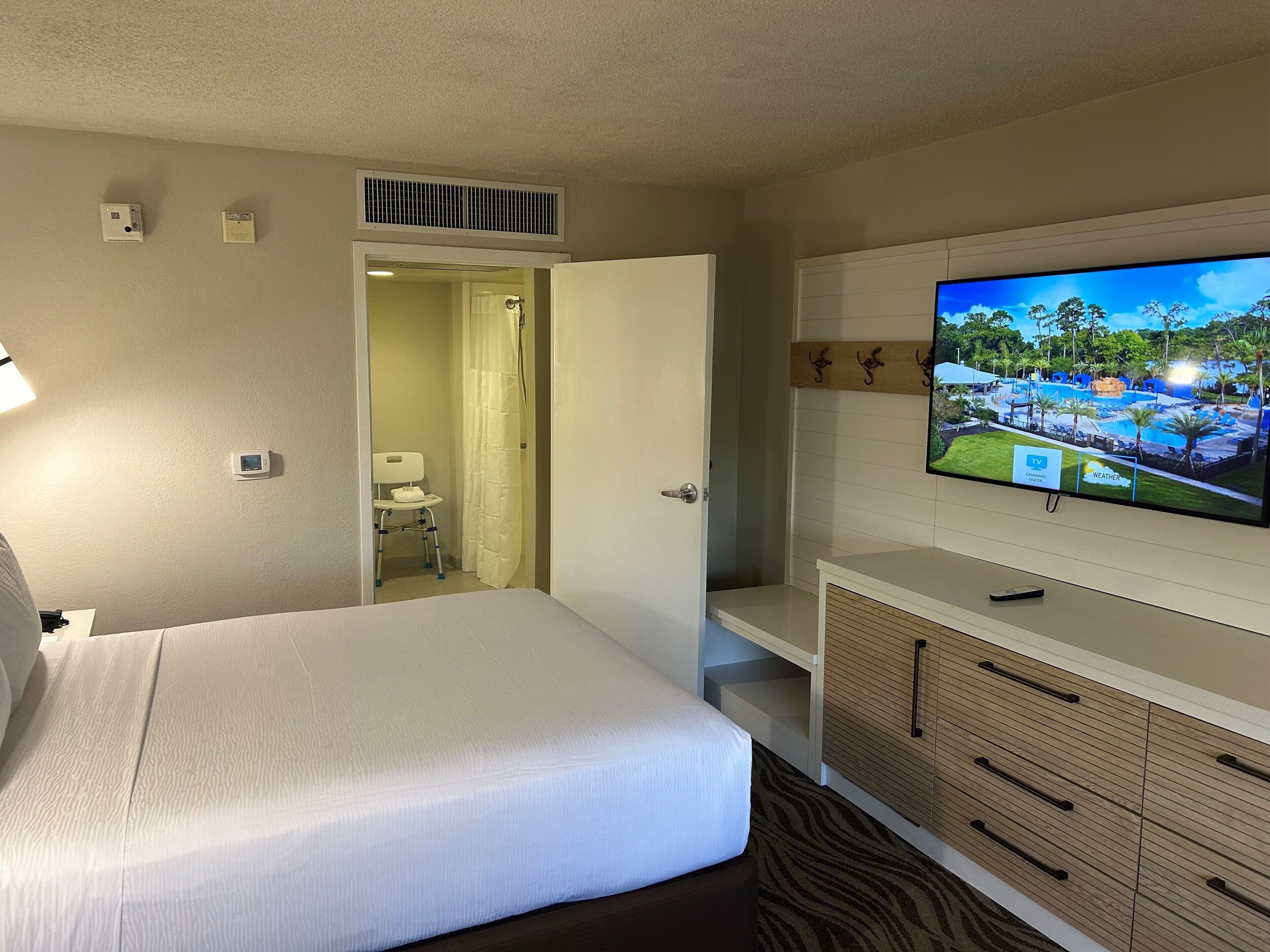 A hotel room with a bed, a TV, a bathroom, and a view of a pool.