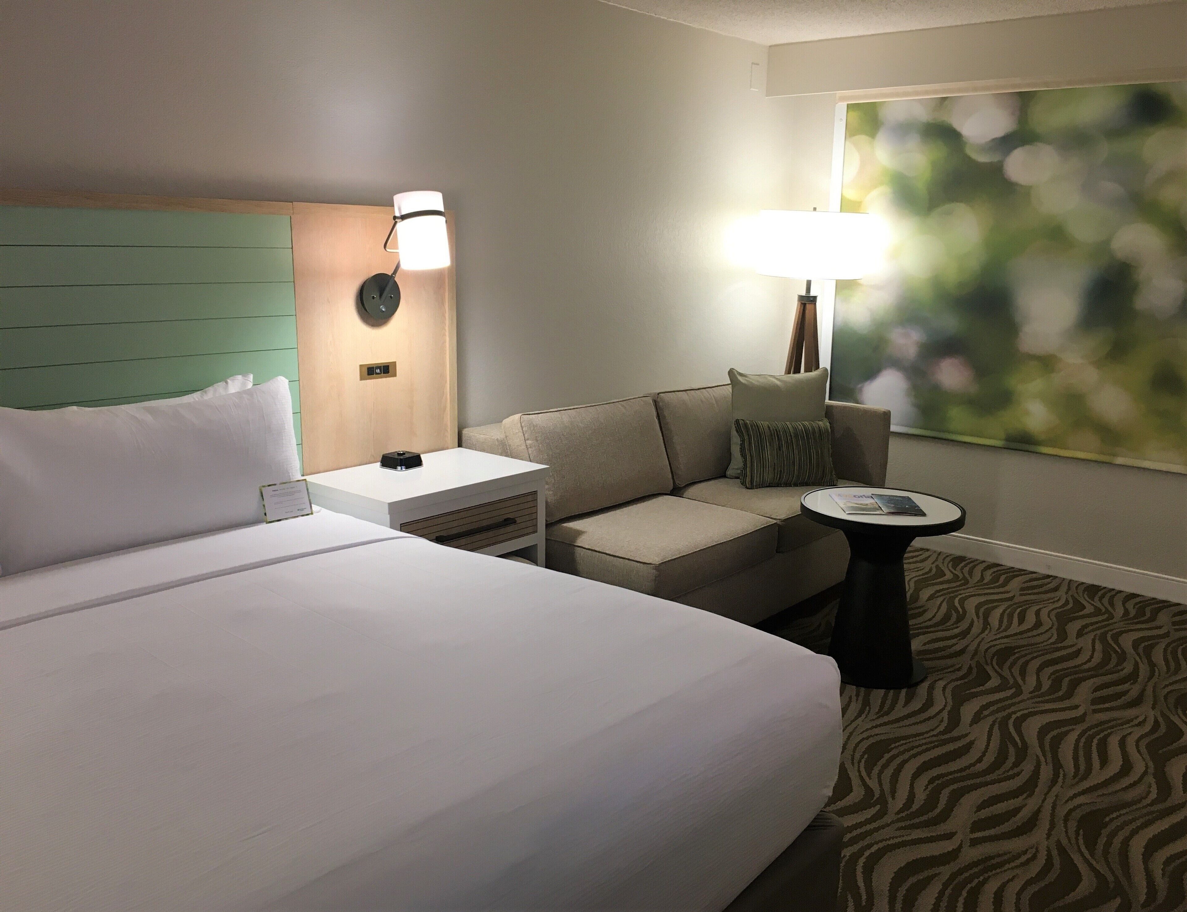 Ein Hotelzimmer mit einem großen Bett, einer Schlafcouch, einem kleinen Tisch und einer Lampe.