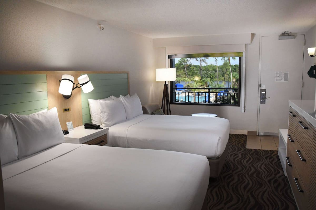 Relax in a stylish room with two single beds, a bedside table, and a large window offering a view of the pool and palm trees.