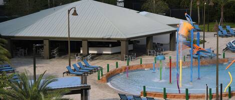 A covered pool area with lounge chairs and a water play structure.