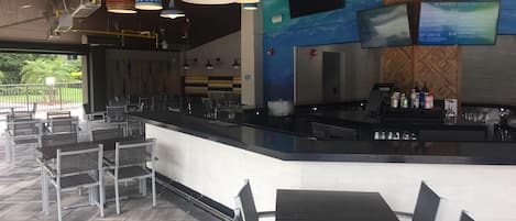 A restaurant with a bar area, tables, chairs, and hanging pendant lights.
